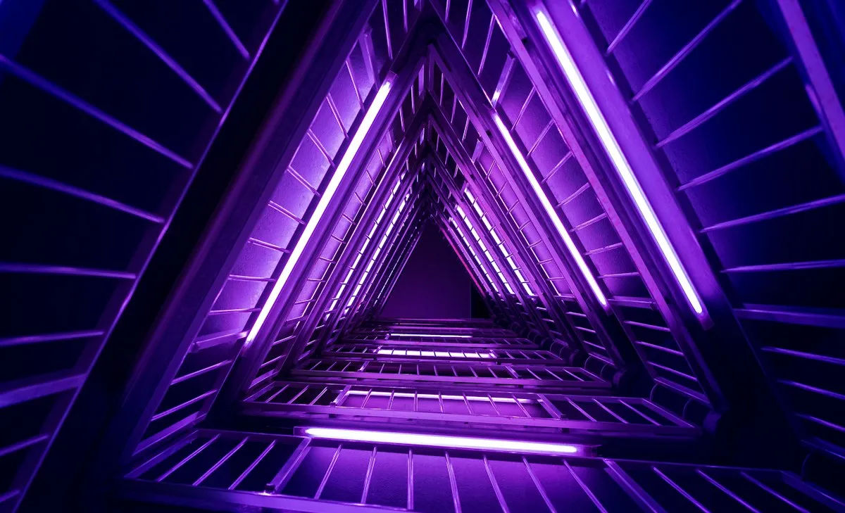 Looking up a triangular stairwell lit with purple neon
