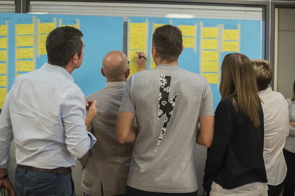 A small team, backs to the camera, working at a wall covered in yellow sticky notes