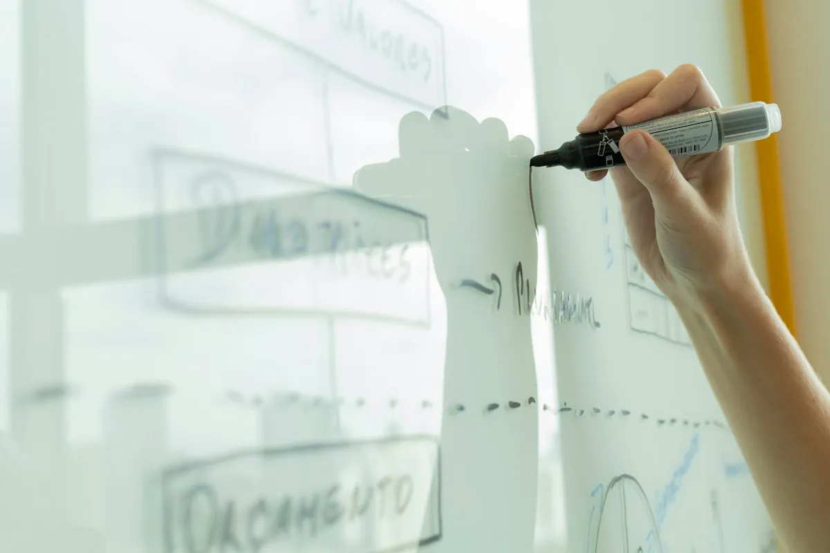 A hand drawing a diagram on a whiteboard with a black marker