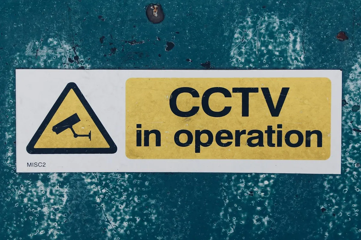 A warning sign reading CCTV in operation, yellow and white on a weathered blue wall